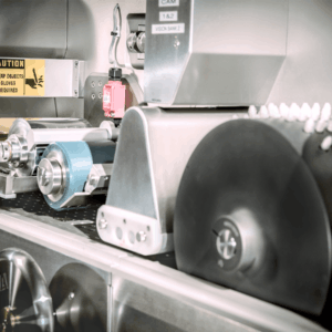 Close-up of the cantilever printing machine with metal rollers and parts, a caution sign warning to wear gloves, and a red emergency stop button visible in the background.