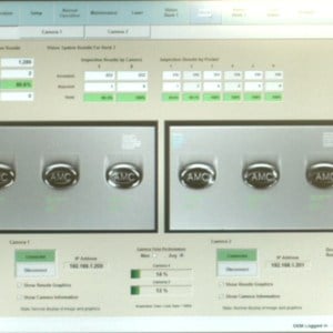 A computer screen displays a vision inspection system for pharmaceuticals, featuring multiple panels, buttons, and graphs. Two large sections in the center show metallic objects labeled "AMC" with status indicators beneath each.