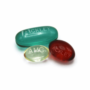 Three oval gelatin capsules in green, yellow, and red, each with laser engraved text. The green capsule reads "ACKLEY," the yellow reads "AMC," and the red reads "ACKLEY," all on a white background.