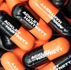 sample model c ink printed dual-color capsule in orange and black with white text sating ackley hartnett